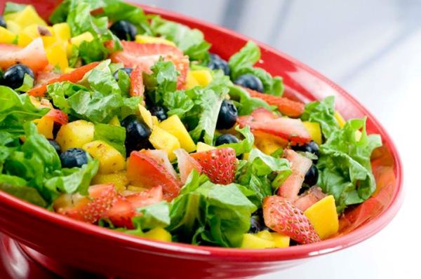 Piros tányéron friss saláta zöldségekkel, olivával, eperdarabokkal.