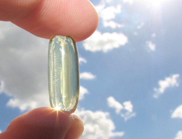 D-vitamint tartanak két ujj között, a háttérben szikrázó napsütés.
