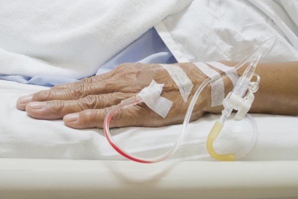 Kórházi ágyon fekvő hölgy kezéből állnak ki mindenféle csövek: infúzió, kanül.