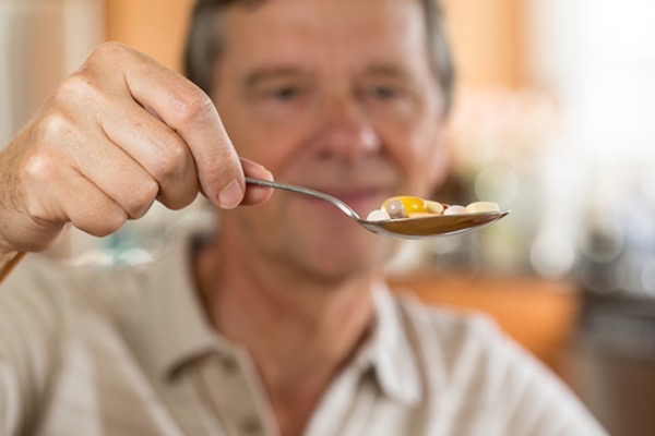 Idősebb férfi egy evőkanálnyi vitamint tart kezében.
