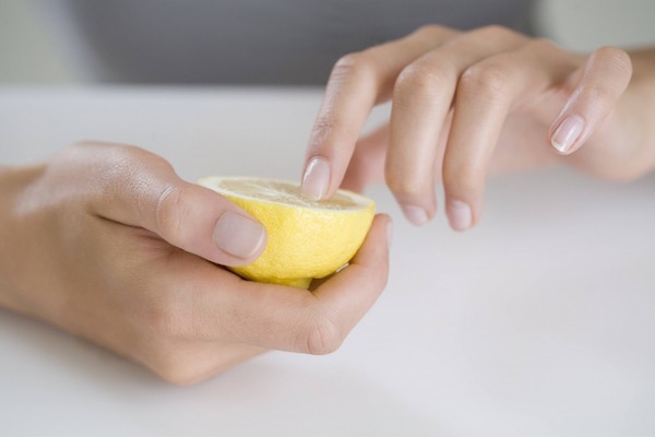 Szépen manikűrözött kezével egy félbevágott citromot tart egy hölgy, így fehéríti mutatóujja körmét.
