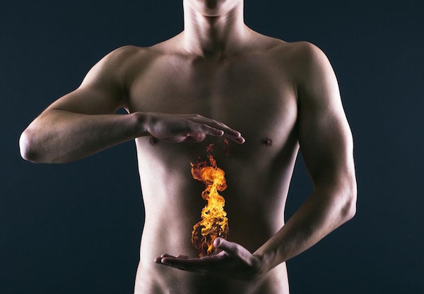 Férfi két keze közt mellkas alatt tüzet ábrázoló kép, mely a gyomorégésre utal.