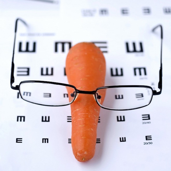Látást ellenőrző kontrollvizsgálat papírlapjára téve egy sárgarépa, rajta egy szemüveg.
