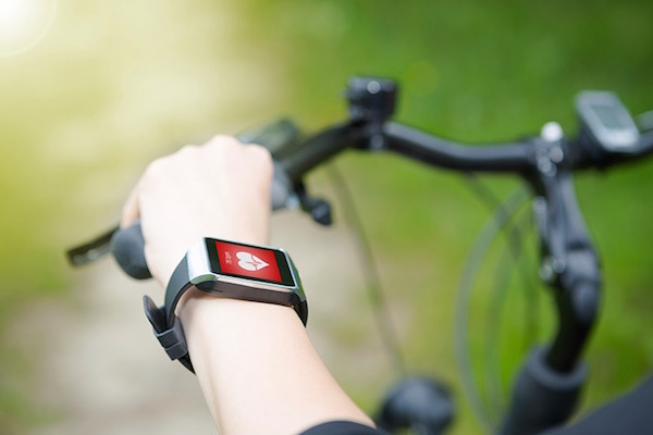 Bicikliző nő kezén egy pulzusmérő óra szív ikonnal.