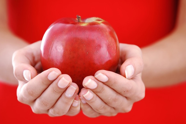 Egy szép piros almát tart kezei között egy piros ruhás lány.