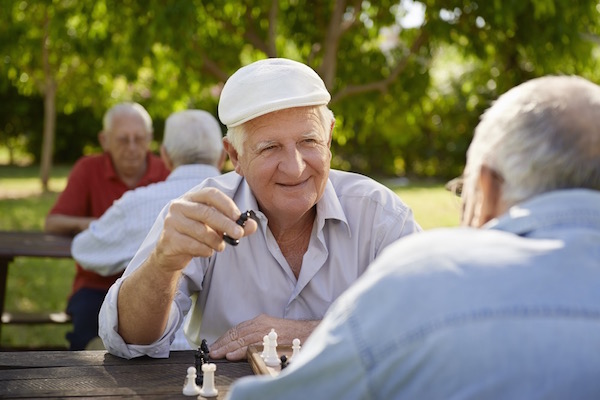 Egy parkban idős emberek sakkoznak a kinti asztaloknál a jó időben.