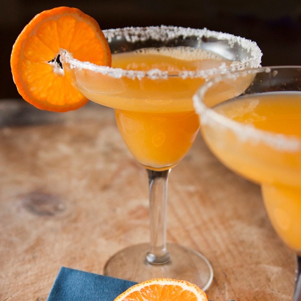 Mandarinos vodkazselé cukrozott szélű széles üvegpoharakba töltve, a pohár szélén egy mandarinszelettel.