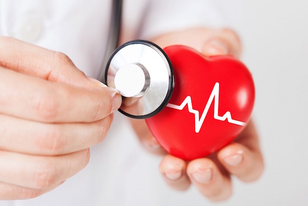 Egy orvos sztetoszkópjával "vizsgál" egy piros műanyag szívet.