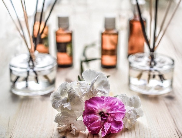 Illóolajok, friss virág, illatpálcák egymás mellett egy faasztalon, az otthoni aromaterápia kellékei.