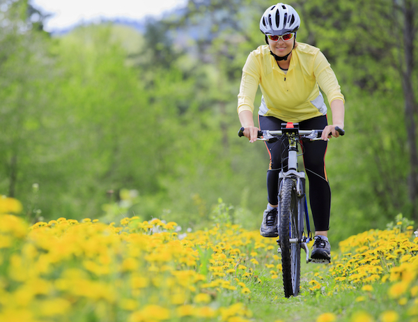 Tavaszi réten kerékpározik egy középkorú nő.