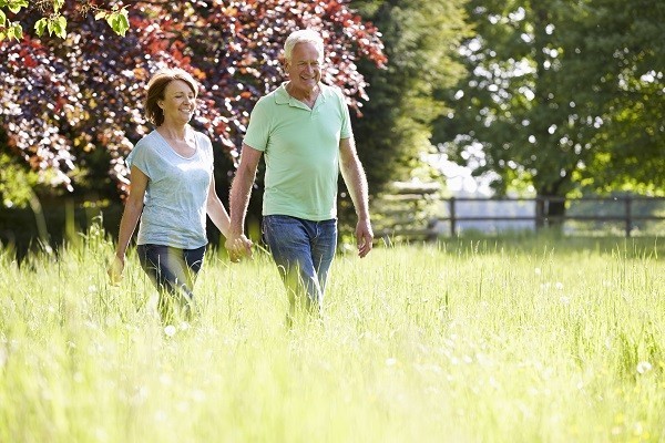Idősödő házaspár kézenfogva gyalogol egy parkban.