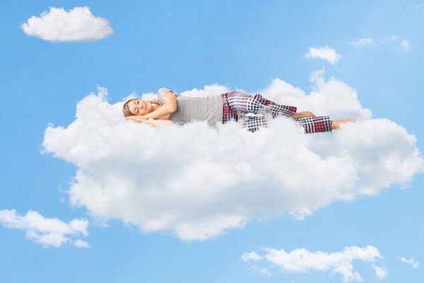 Felhőben alszik egy pizsamát viselő fiatal nő.