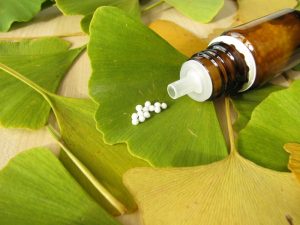 Ginkgo biloba levelei, rajta homeopátiás golyókkal teli üvegcse, az egyik levélen pár szem gyógyszer.