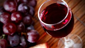 Üvegpohárban lévő vörösbor, mellette nagy fürt szőlő.