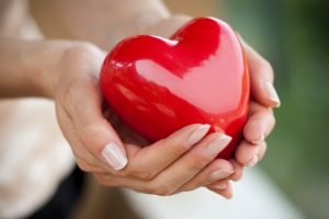 Piros műanyag szívet tart egy női, ápolt kéz két tenyerében.