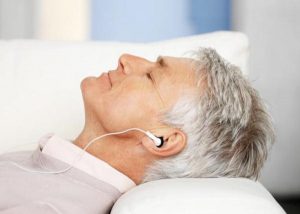 Ősz hajú idősebb férfi kanapén fekve fülhallgatóján keresztül zenét hallgat.