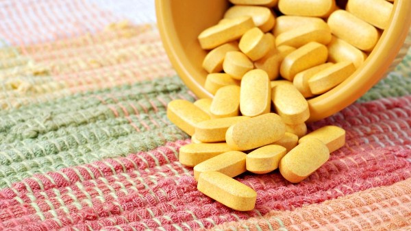 Sárga színű tabletták kiöntve egy hasonló színű edényből egy csíkos rongyszőnyegre.