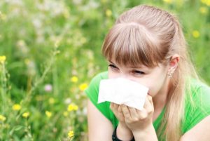 Virágos, zöld mezőben egy fiatal lány papírzsebkendőbe tüsszög.