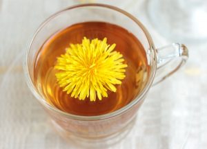 Pitypangtea üvegpohárban felülről fotózva, a tea közepén a növény sárga virága.