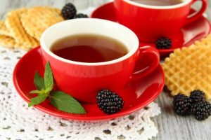 Piros csészében földi szederből készült tea, a csészaljon egy szem szeder és friss levélhajtások.