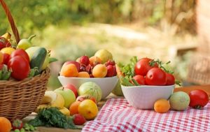 Piros kockás abrosszal leterített kerti asztalon kosárban, tálakban friss zöldségek és gyümölcsök.