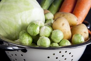 Zománcozott szűrőben téli zöldségek: káposzta, kelbimbó, sárgarépa és krumpli.