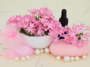 Verbéna apró virágai, mellette egy belőle készült szappan, fehér gyöngyök és illóolajas üvegcse.