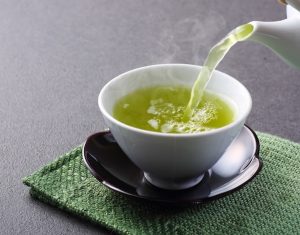 Forró zöld teát öntenek porcelán teáskannából egy csészébe.