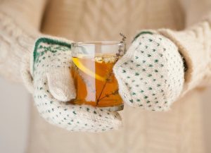 Gyógynövényes teát fog jó melegen felöltözve valaki, kezén vastag, mintás egyujjas kesztyű.