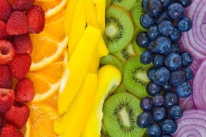 Különféle színű gyümölcsök és zöldségek egymás mellé szín szerint rakva: málna, narancs, citrom, kivi, áfonya és lila hagyma.