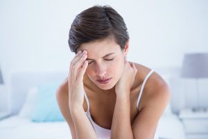 Középkorú nő az ágyán ülve migréntől szenved.
