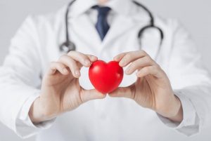 Fonendoszkópot viselő orvos egy piros műanyag szívet tart a kezei között.