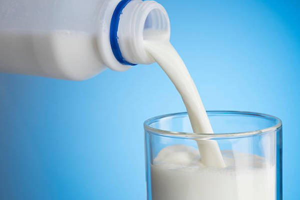 Műanyag flakonból tejet töltenek egy üvegpohárba.