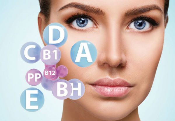 Bőrre ható különféle vitaminok betűjelei egy női arc mellett.