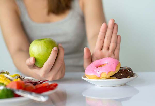 Cukros fánkot utasít el egy almát kezében tartó fiatal nő.