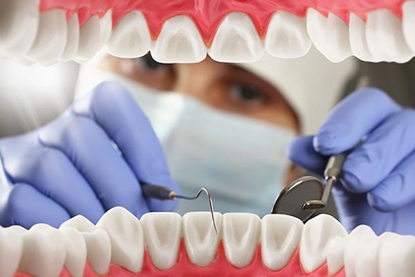 Műanyag fogsor makettet vizsgál egy lila gumikesztyűs fogorvos.