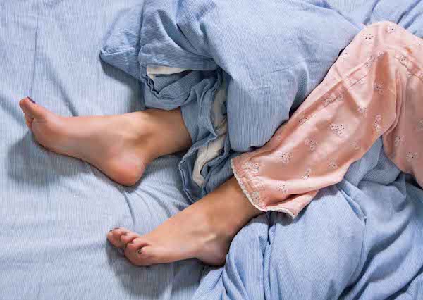 Hölgy pizsamás lába az ágyban.