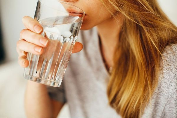 Fiatal hölgy vizet iszik üvegpohárból.