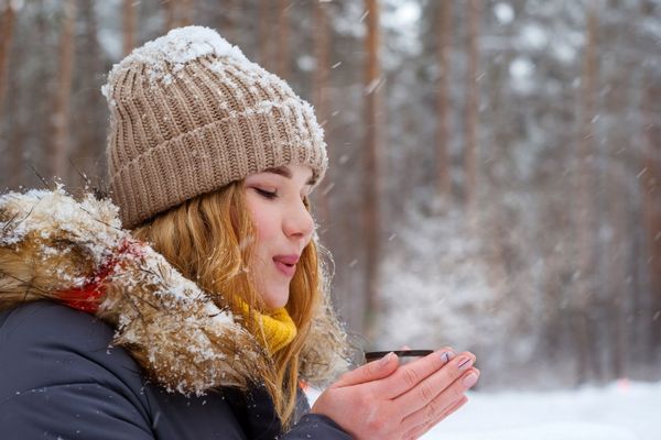 Fiatal lány télen havas erdőben forró teát iszik.