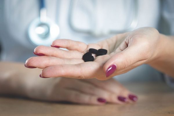 Egy hölgy aktív szén tablettákat tart a kezében.