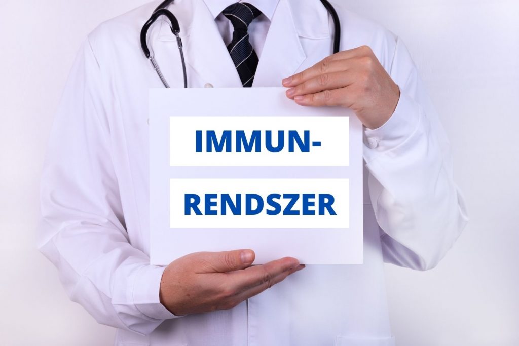 Egy fehér köpenyes orvos egy táblát tart a kezében, amelyen Immunrendszer kifejezés olvasható.