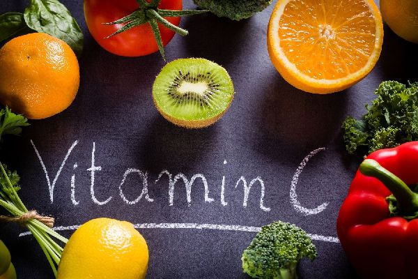 Egy sötét színű asztalon C-vitamin-felirat, körülötte kivi, narancs, paradicsom, brokkoli, paprika, citrom, spenót.