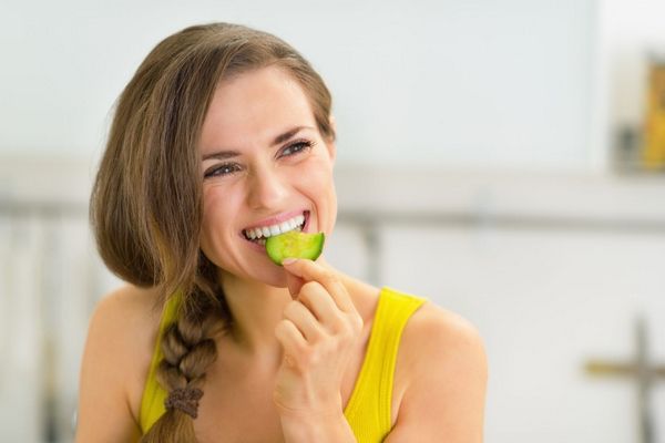 Egy fiatal nő sárga trikóban mosolyog és uborkát eszik.