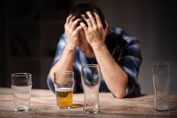 Egy férfi asztalnál ülve fejét a kezeibe temetve ül, előtte üres alkoholos poharak és sörös pohár.