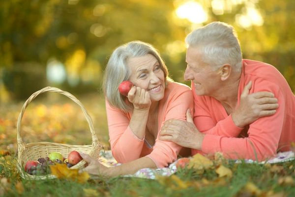 Egy idős, nyugdíjas házaspár a fűben feküdve egymásra mosolyog.