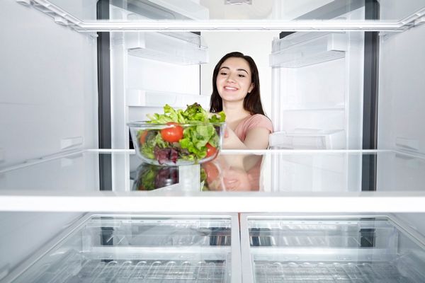 Egy fogyókúrázó lány hűtőszekrénybe nyúl, üres hűtőszekrényben csak egy tál saláta van.