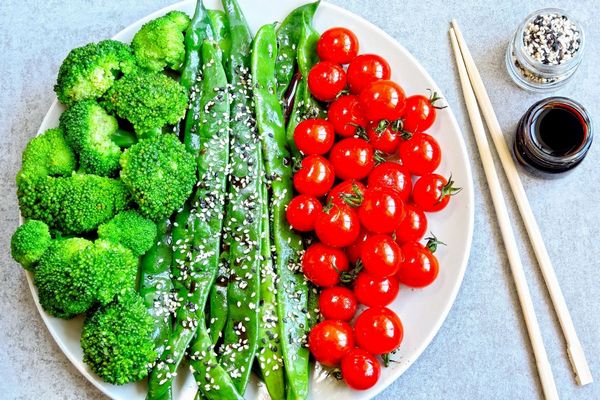 Egy tányéron brokkoli, koktél paradicsomok, zöldbabok, mellettük salátaöntet kis üvegben.