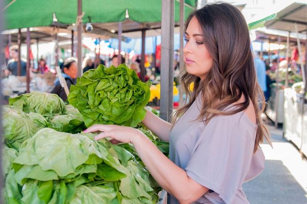 Egy piacon a zöldségesnél egy nő salátát válogat.