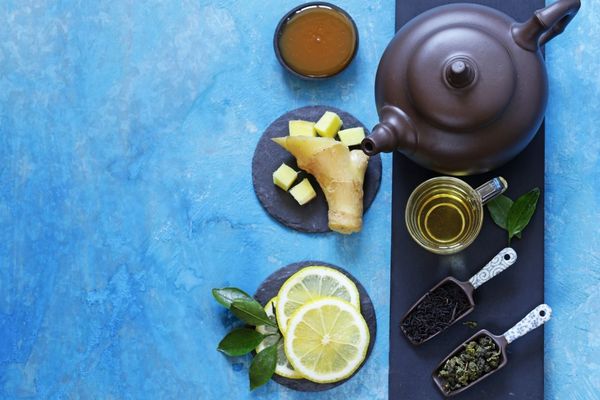 Egy kék asztalon barna teáskanna, citromkarikák, gyömbér, zöld tea üveg pohárban, méz.