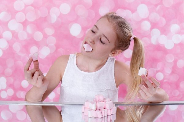 Egy rózsaszínű háttér előtt egy kislány rózsaszínű cukorkákat eszik.
